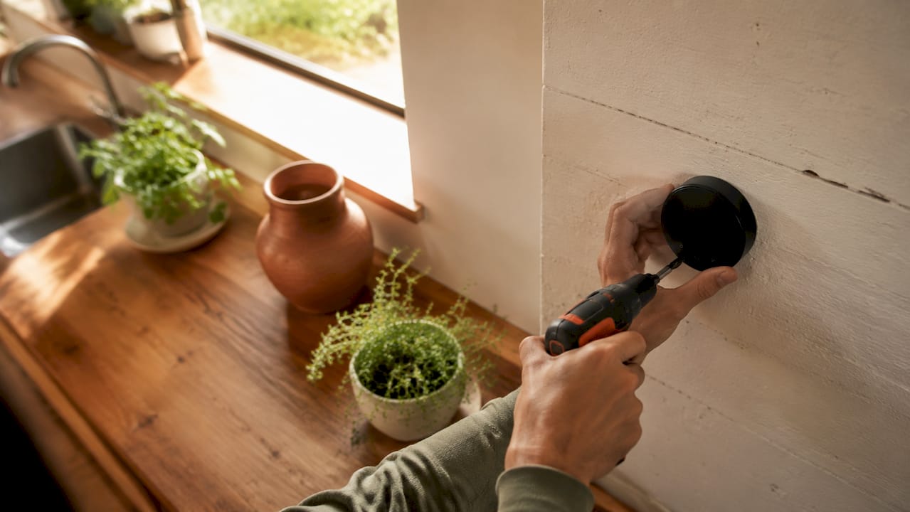 Hands installing modern smart thermostat on wall