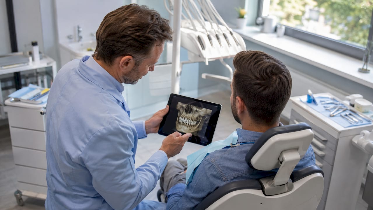 Der Zahnarzt zeigt seinem Patienten auf dem Tablet, wie der dreidimensionale Kieferscan funktioniert.