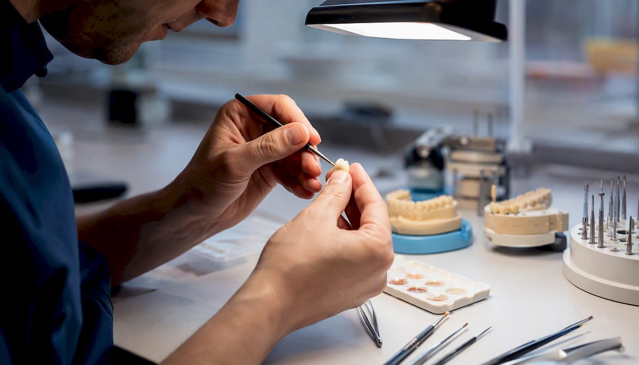 Izkušene roke natančno oblikujejo zobno krono v laboratoriju, da bo popolno pristajala pacientu.