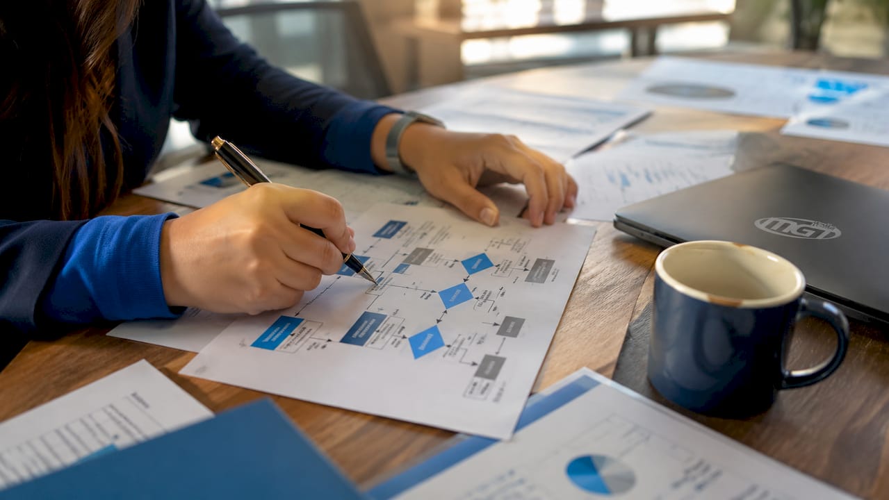 Mani che prendono appunti su uno schema di lavoro per la gestione dell’inventario in ufficio.