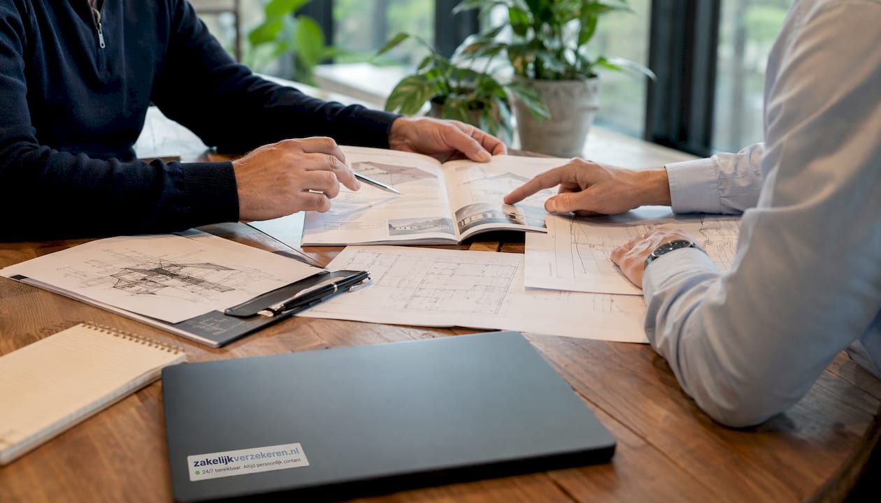 Twee paar handen wijzen en gebaren boven stapels papieren terwijl ze samen de verschillende manieren van vastgoedwaardering bespreken.