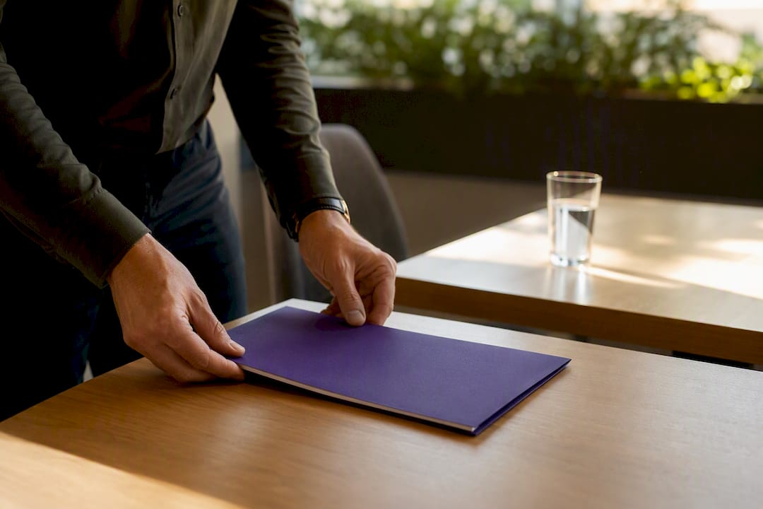 Twee handen leggen een uitnodigingsmap voor een mediation op tafel.