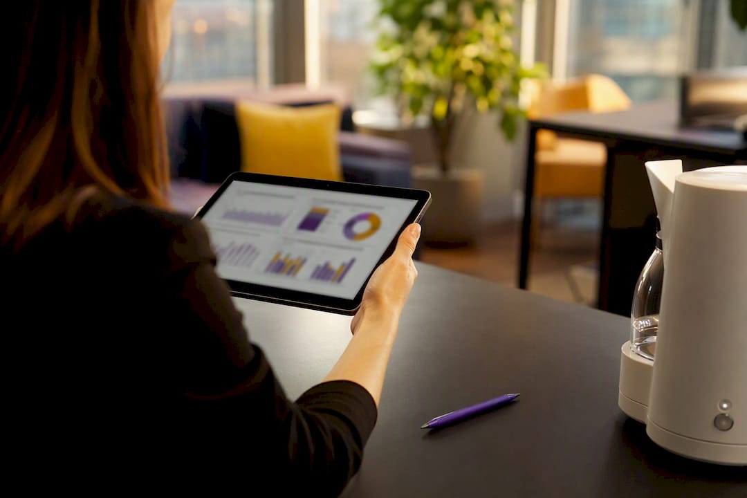 Hand die met een vinger wijst naar wazige grafieken op een tablet met een koffiekopje erbij