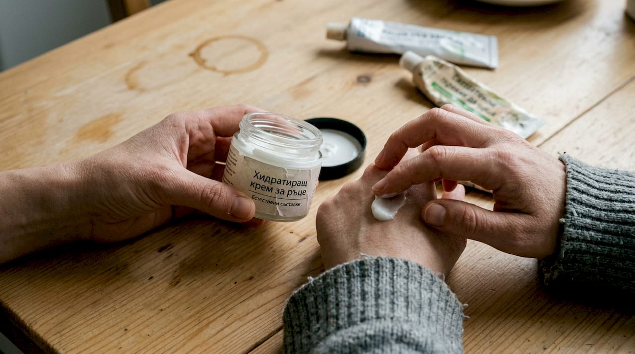 Докато си седя на кухненската маса, нанасям крем на ръцете си.