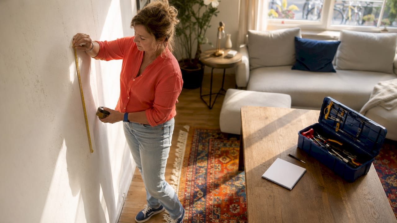 Een vrouw verricht tijdens een bouwkundige keuring metingen aan een binnenmuur.