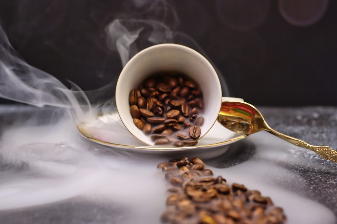 Coffee beans spilling from an overturned cup with steam.