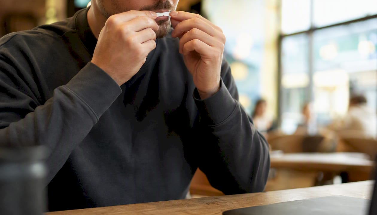 Hands discreetly placing nicotine pouch inside mouth on bus