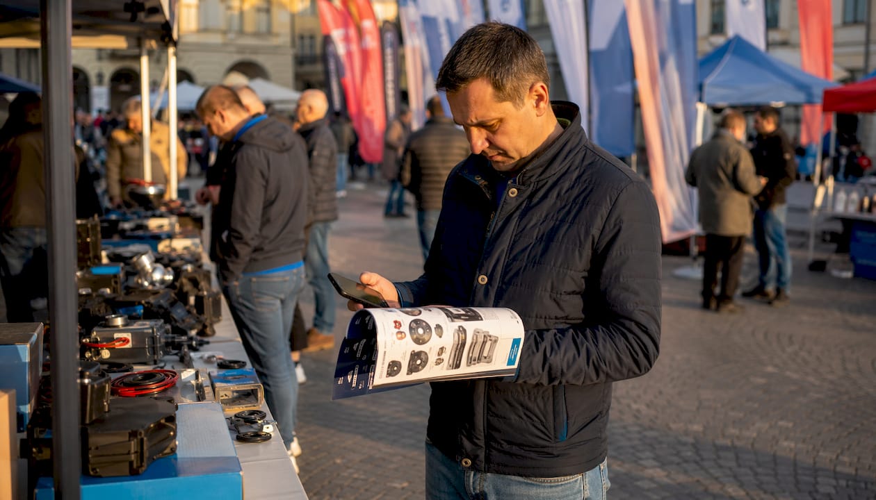 Stranka v trgovini primerja različne elektronske naprave in avtomobilske dele ter se odloča, kaj bi ji najbolj ustrezalo.