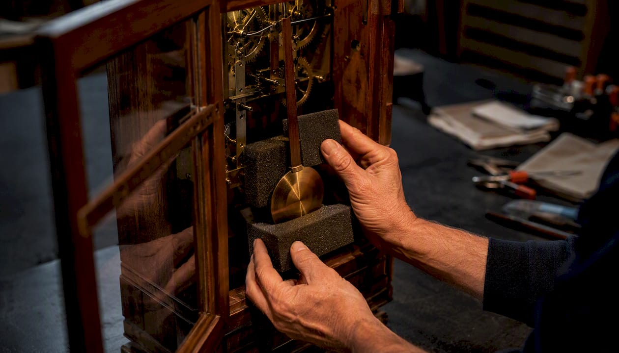 Hands securing pendulum with foam in antique clock