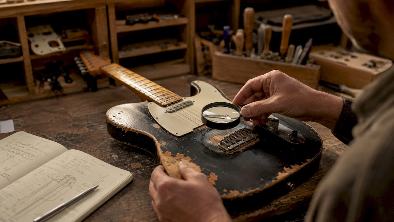Mit den Händen wird die beschädigte Oberfläche der Gitarre begutachtet.