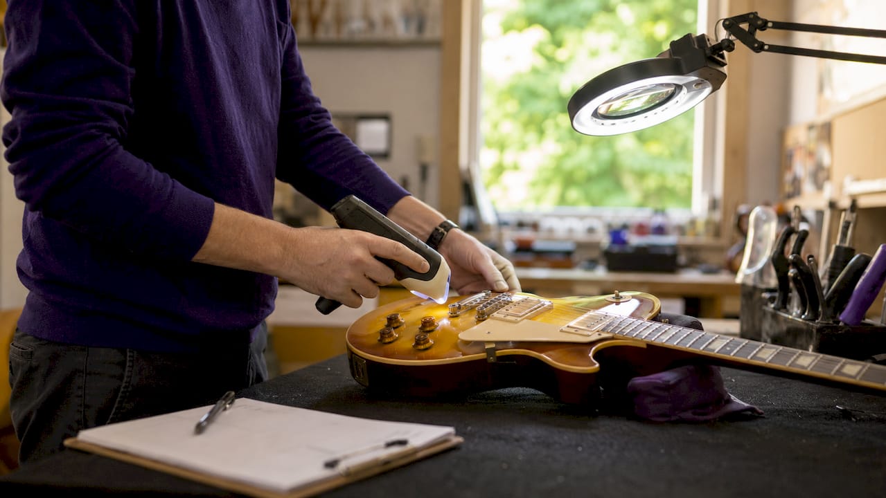 Hands scanning vintage guitar with spectrometer