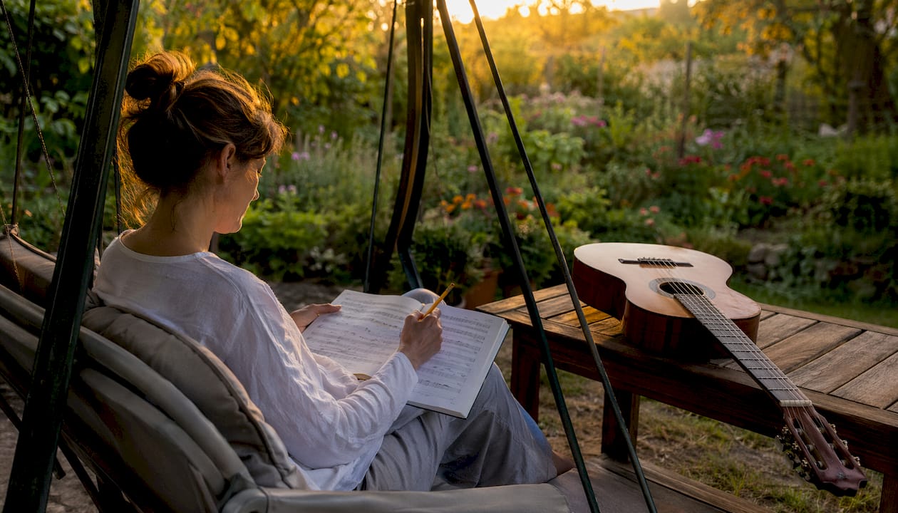 Eine Frau macht sich auf ihren Notenblättern Notizen, um ihre Gitarrenübungen zu verbessern.