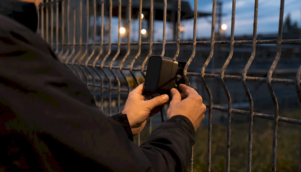 Hands mounting vibration sensor on perimeter fence
