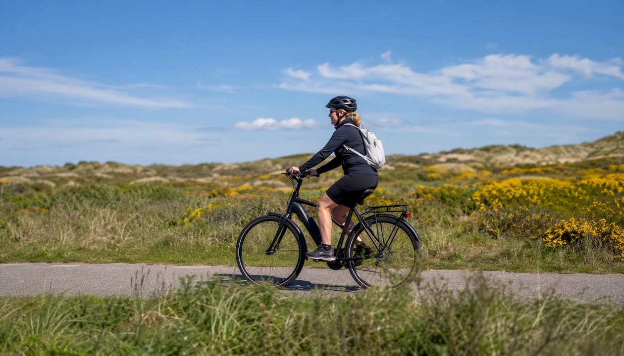 Een vrouw trapt ontspannen door de duinen van Vlieland.
