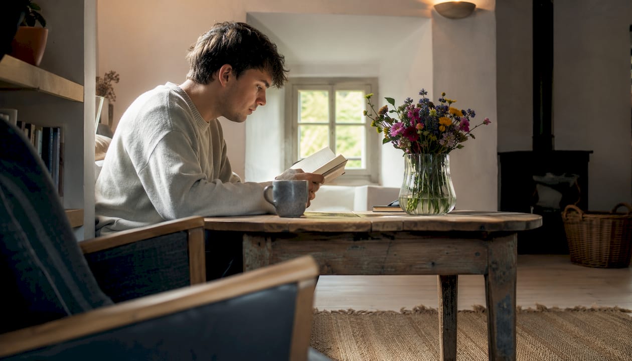 Een man zit ontspannen een boek te lezen in een strak, minimalistisch ingericht interieur.