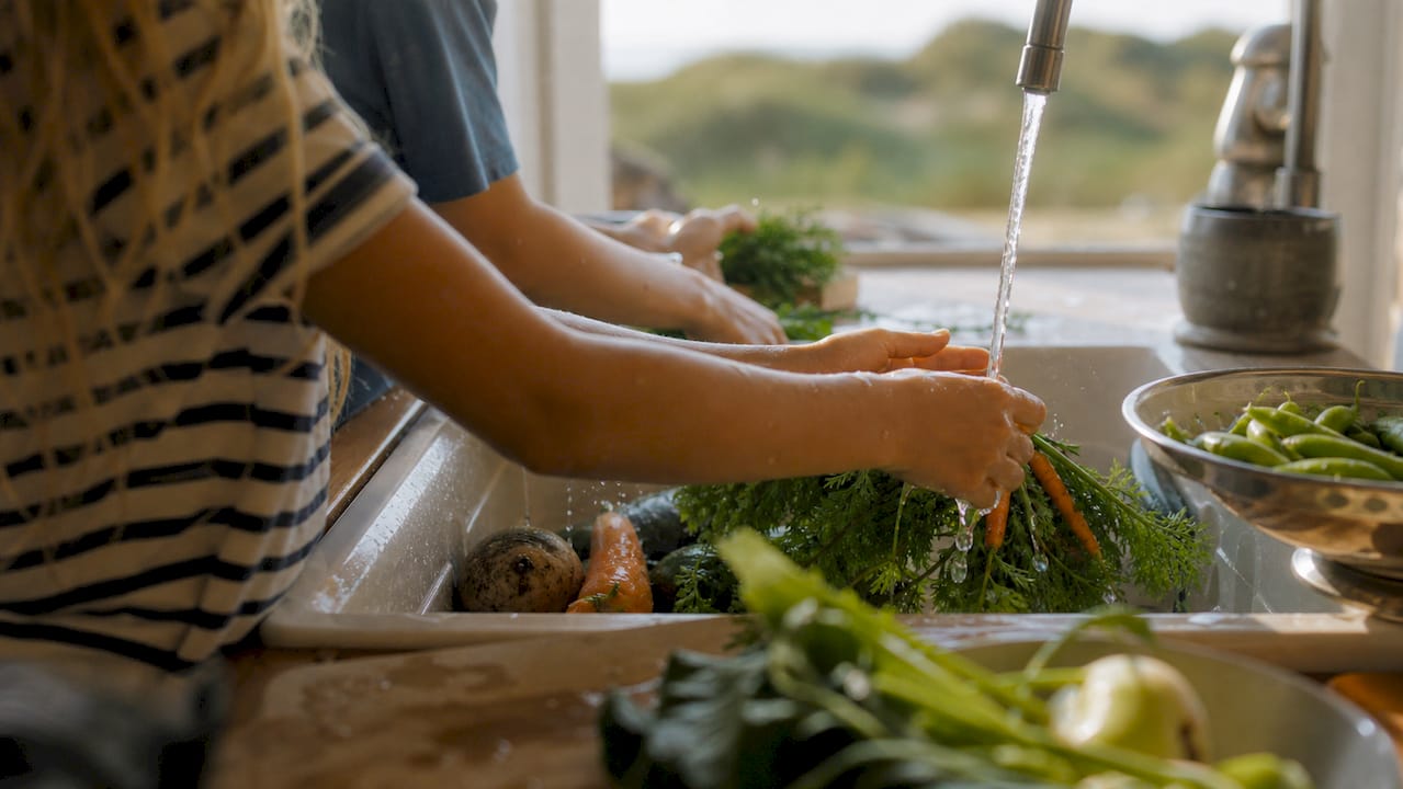 Kinderen staan samen groenten te wassen in de gootsteen van het vakantiehuisje.