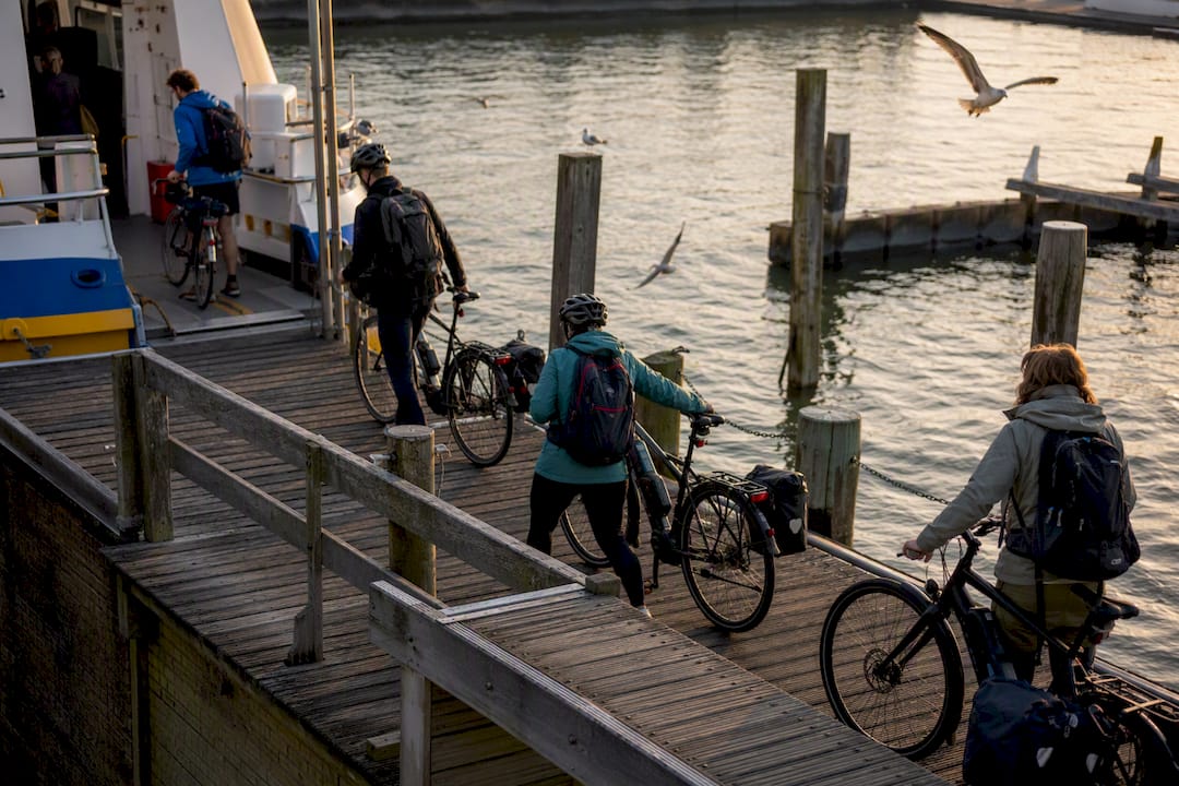 De veerboot legt aan en reizigers halen hun fietsen tevoorschijn om aan wal te gaan.