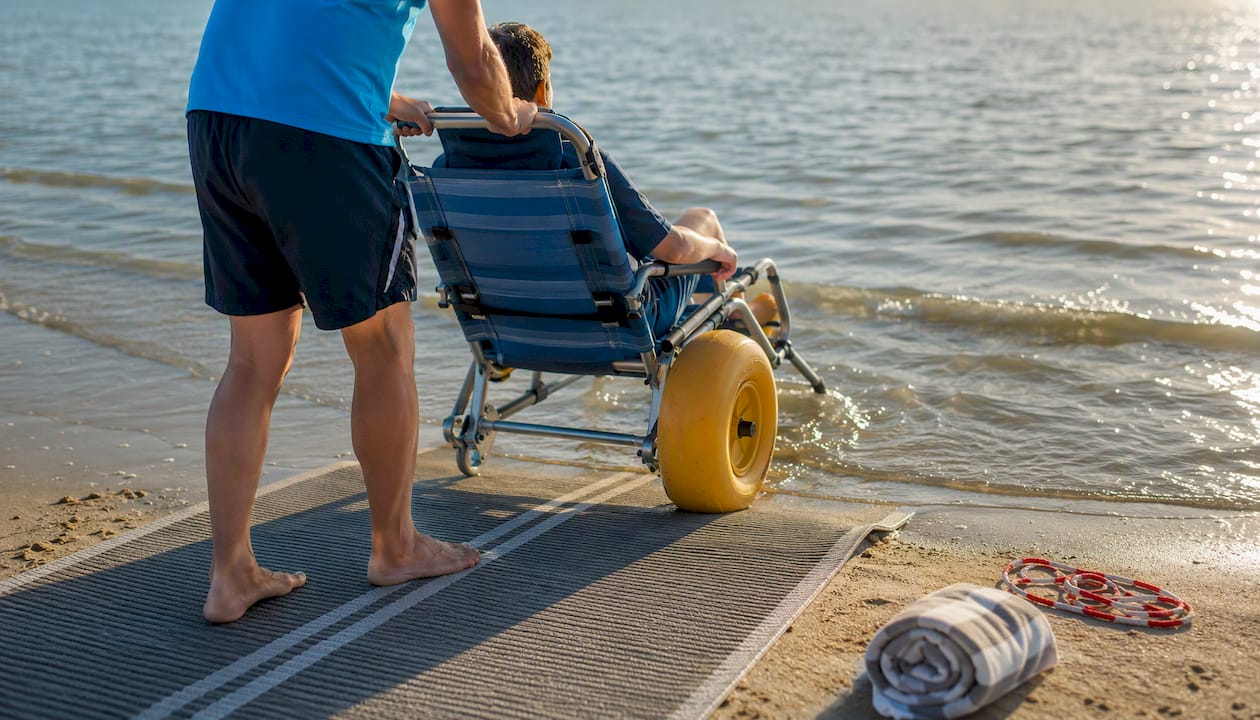Begeleider rijdt met waterrolstoel de branding in