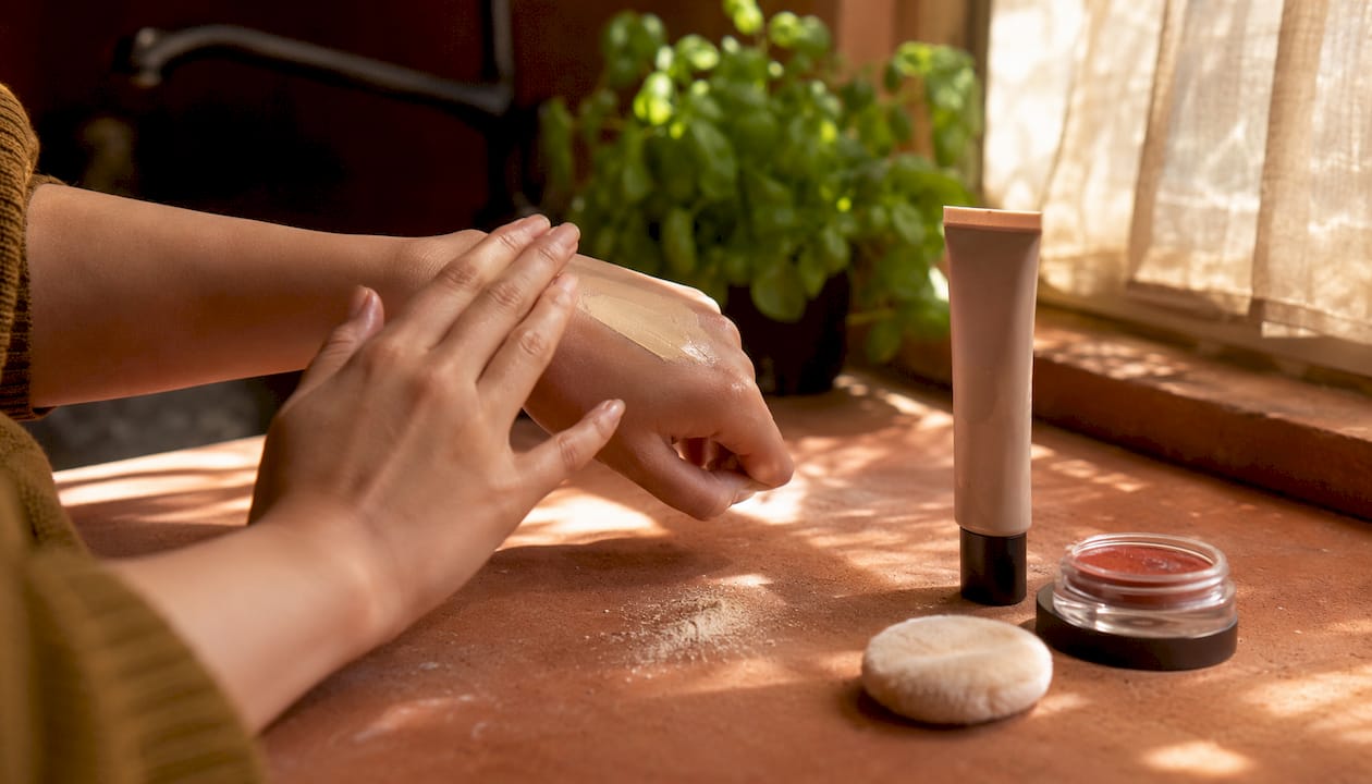 Hands applying cream makeup on skin