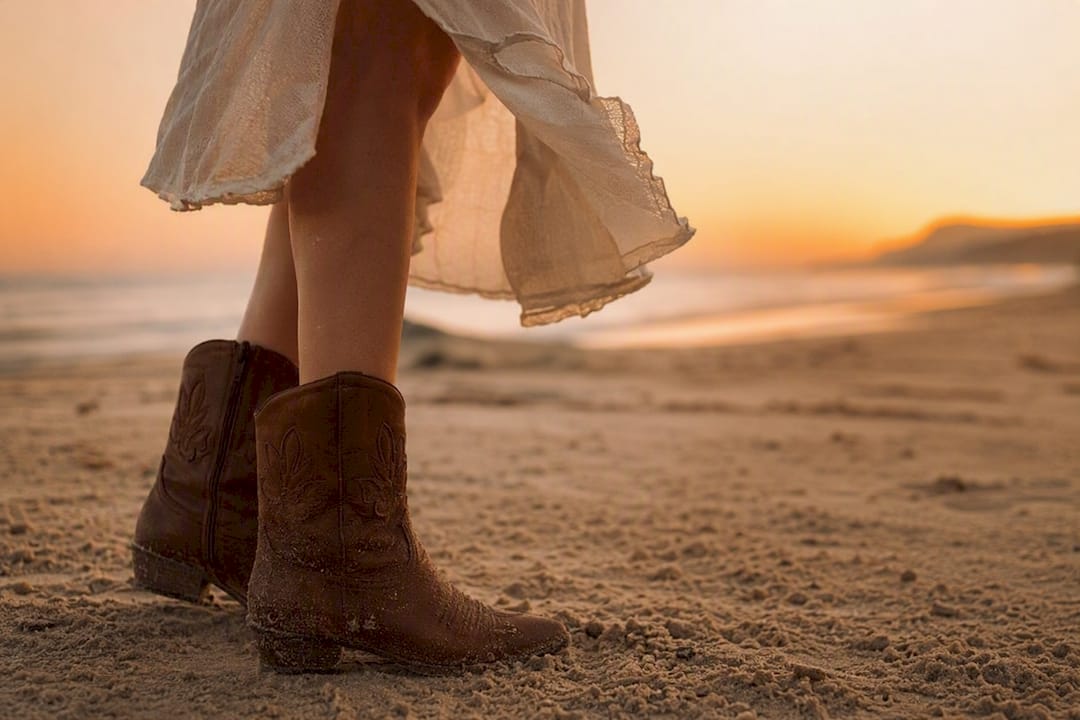 Mid-calf boots and dress on sand close-up