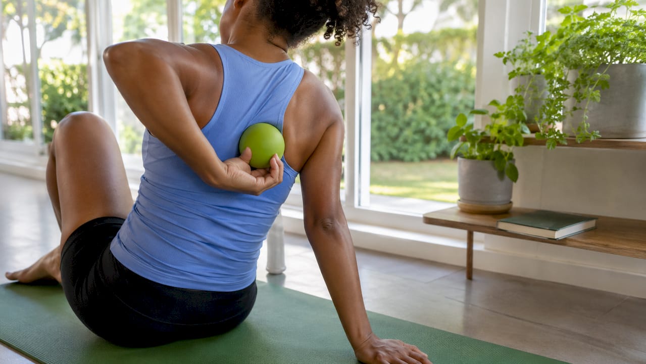 Hands using lacrosse ball on upper back muscles