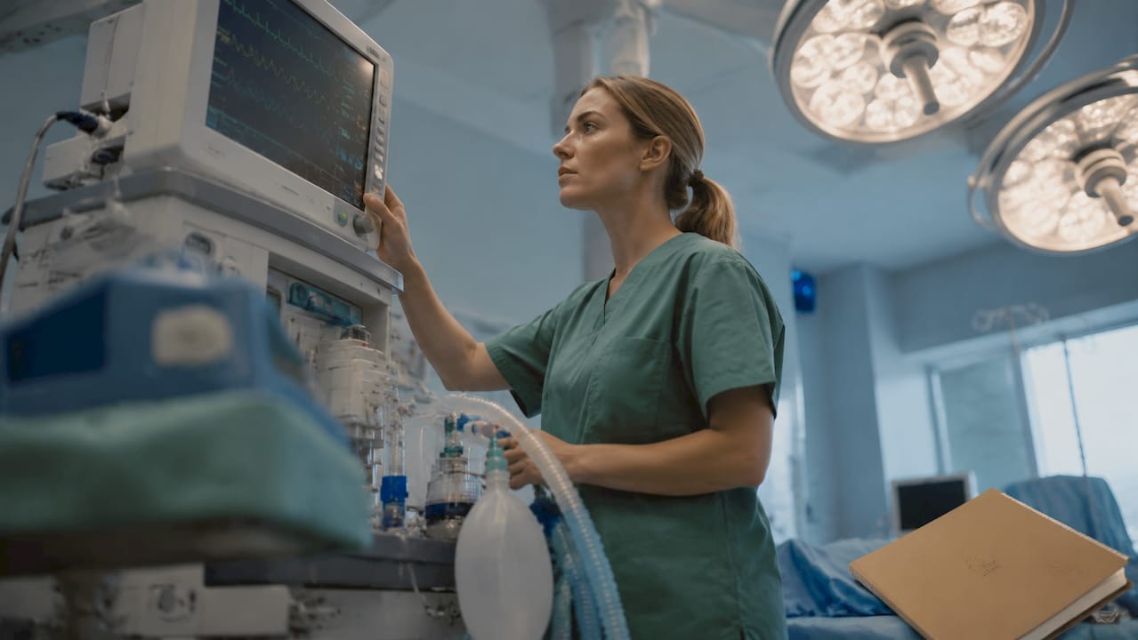 En anestesisjuksköterska som övervakar patientens vitala funktioner med hjälp av avancerad utrustning under operationen.