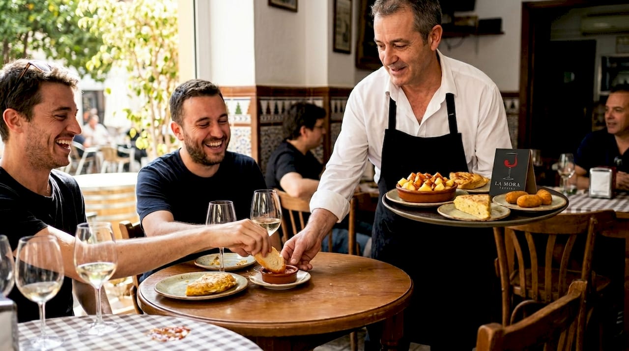Un camarero atiende a los clientes en la terraza del bar, ofreciendo las tapas de toda la vida.