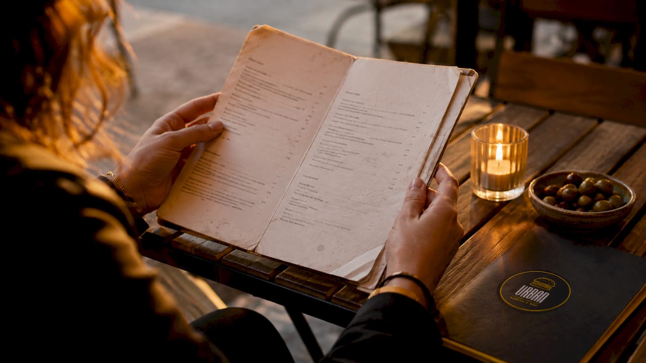 Unas manos hojean la carta en un restaurante con ambiente cálido y agradable.
