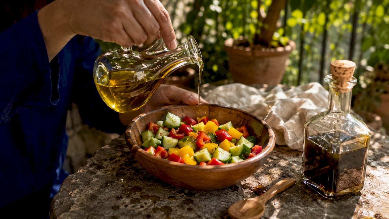 Hands pouring olive oil over Spanish salad