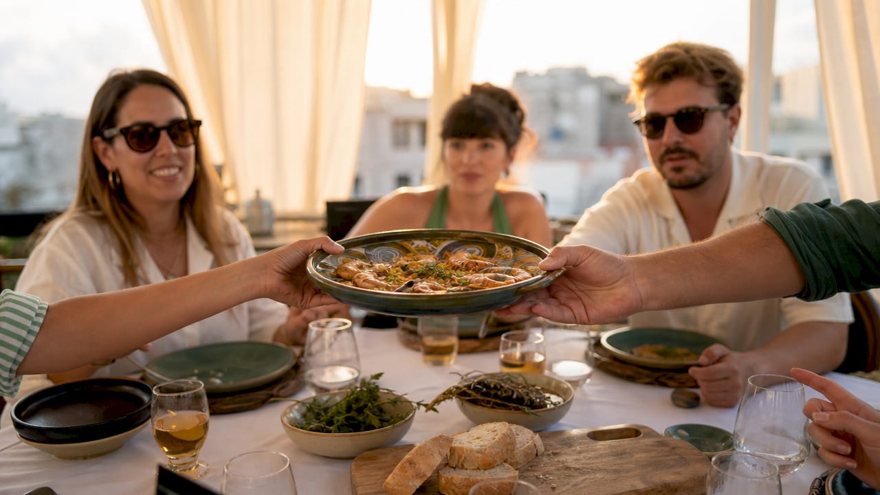 Hands passing shared Catalan dish on table