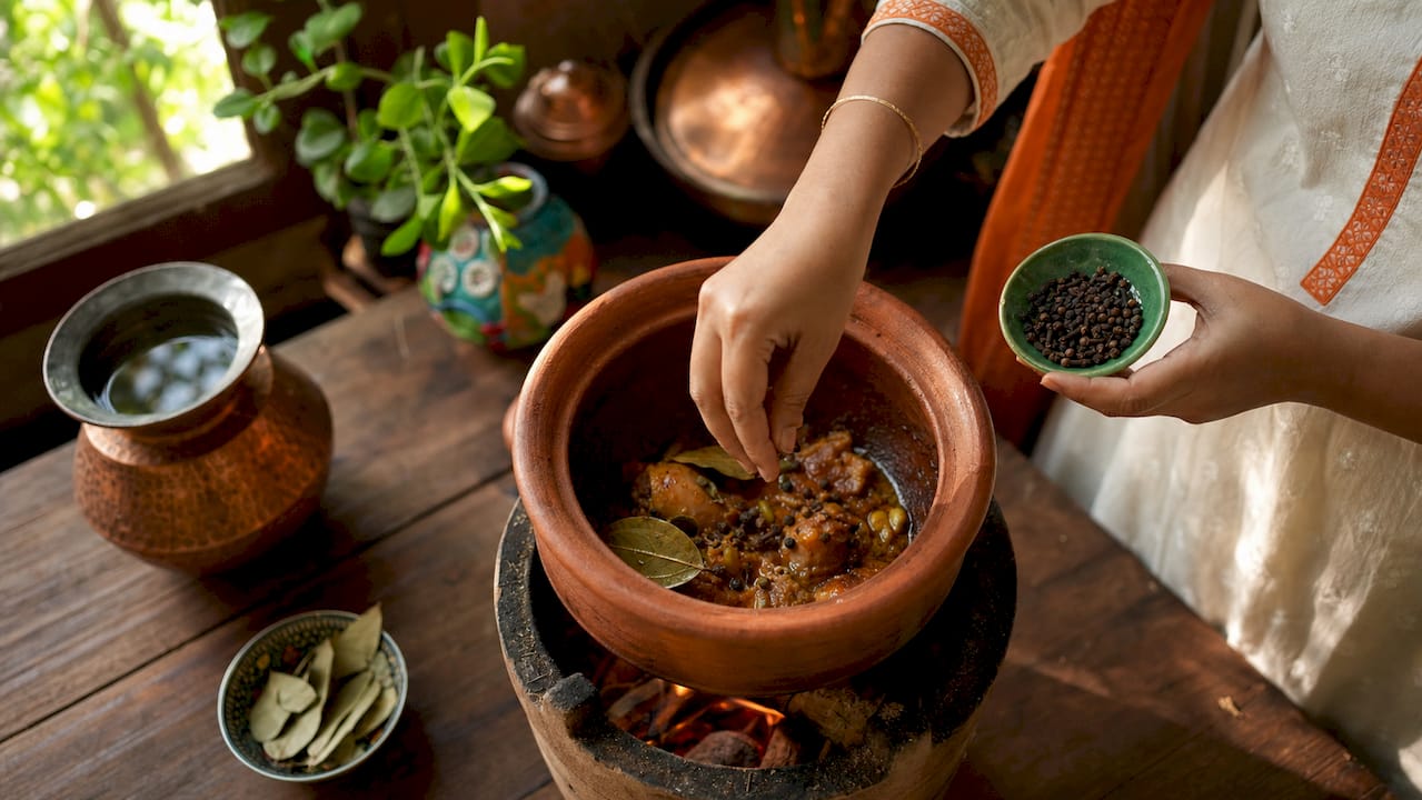 Unas manos añaden especias a una sartén caliente para preparar un curry.