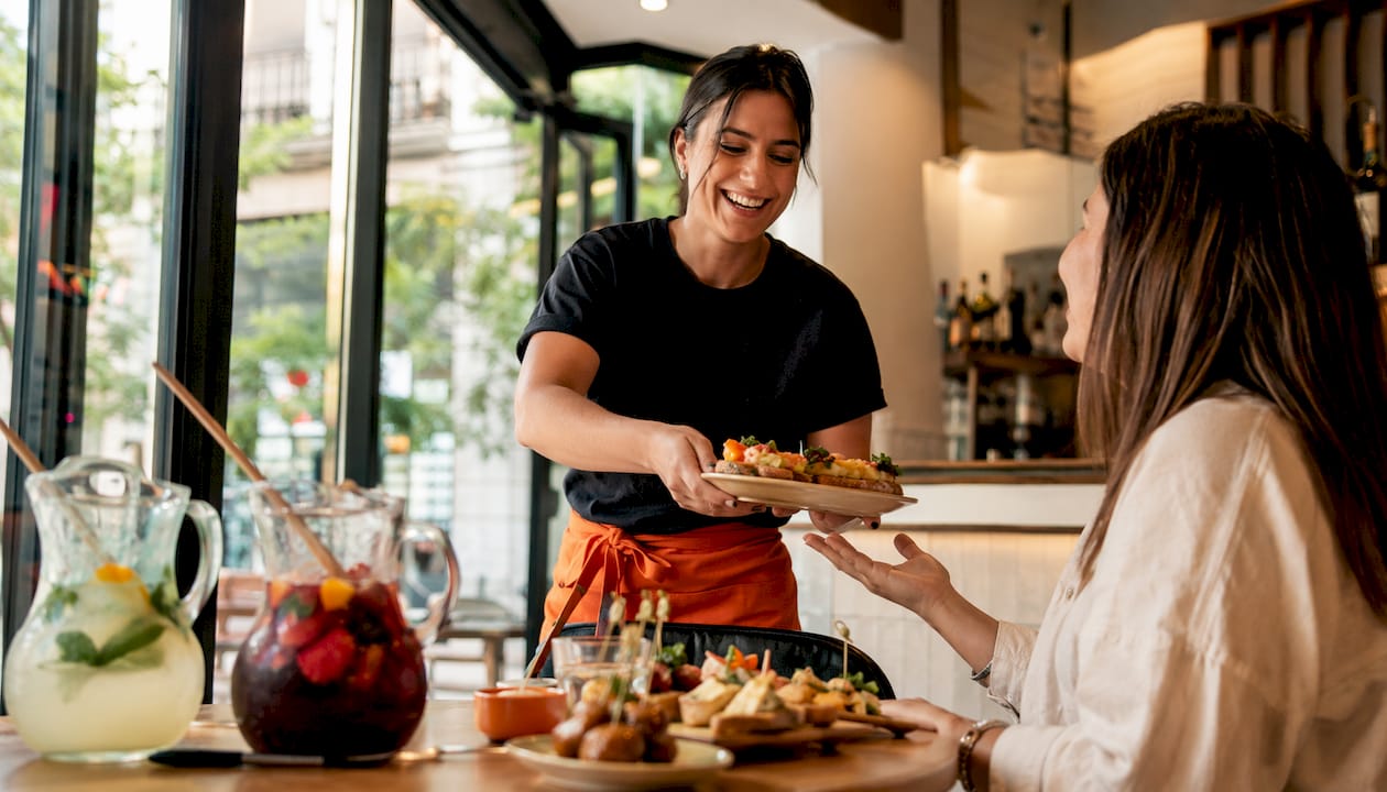 Una camarera atiende a los clientes en un restaurante típico de Barcelona, ofreciendo platos tradicionales y un trato cercano.