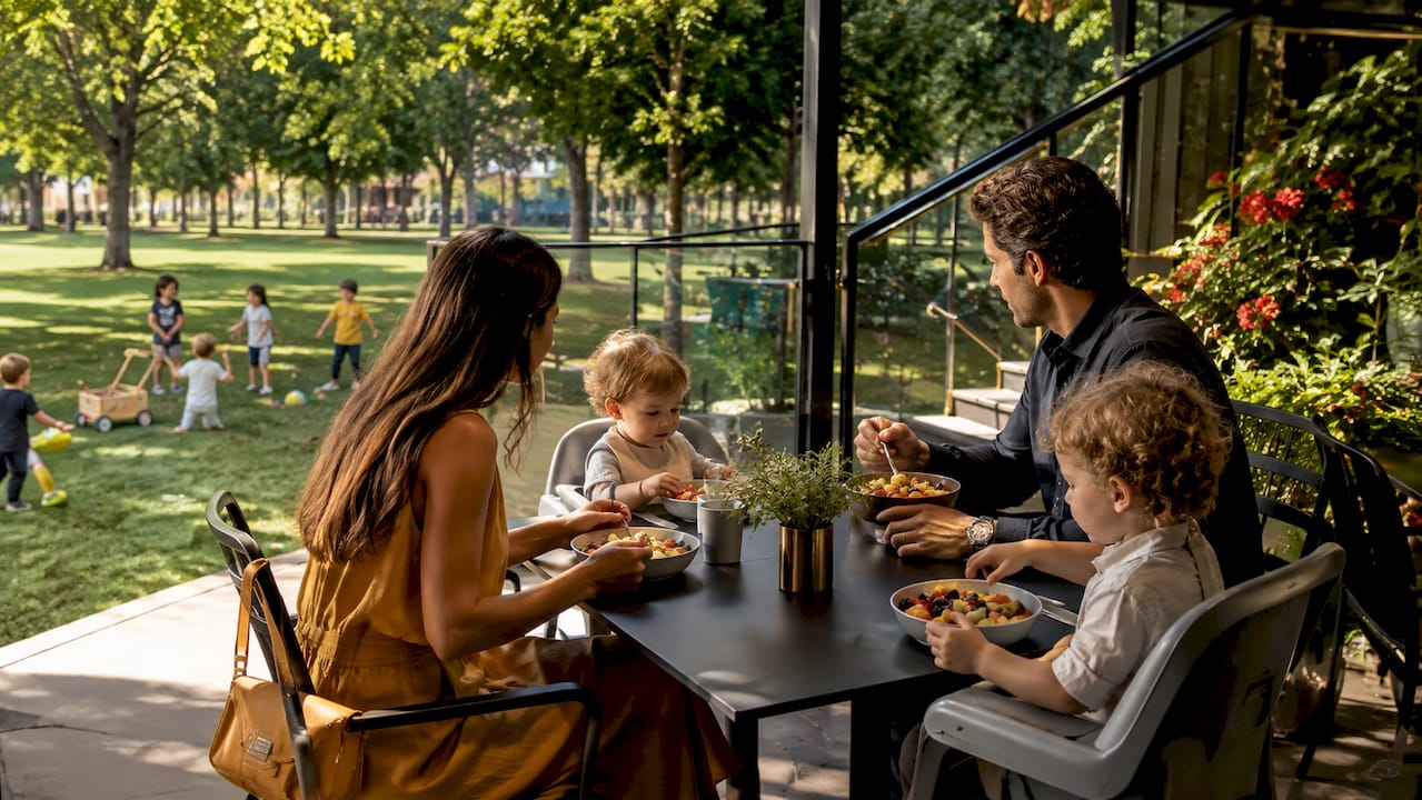 Una familia disfruta de la tarde en una terraza, mientras los niños pequeños juegan alegremente en el parque cercano.
