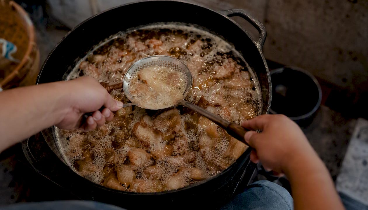 Manos retirando la espuma del manteca mientras se preparan las carnitas