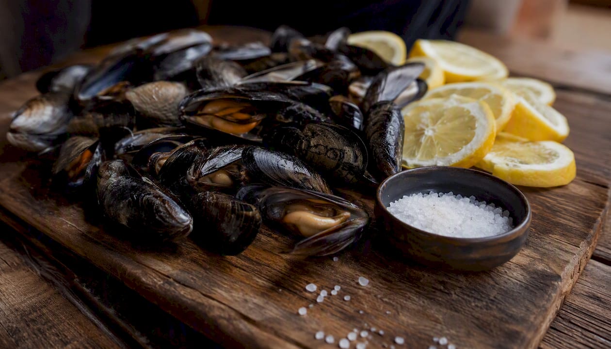 Mejillones frescos servidos con unas gotas de limón y una pizca de sal sobre una tabla de madera
