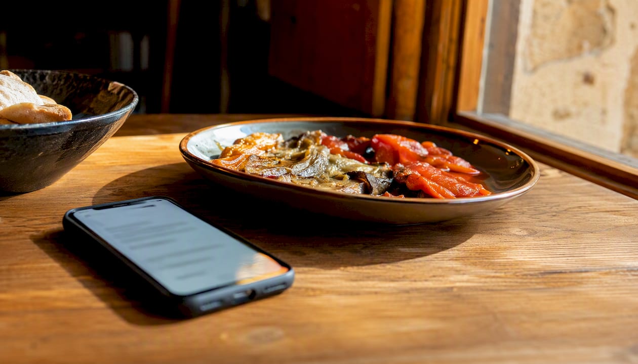 Teléfono móvil junto a una nota vegetariana y un plato de tapas rústicas