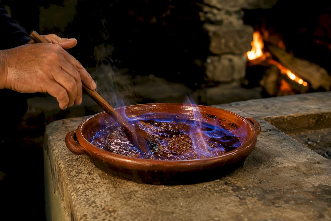 Unas manos remueven la queimada ardiendo en una olla de barro.