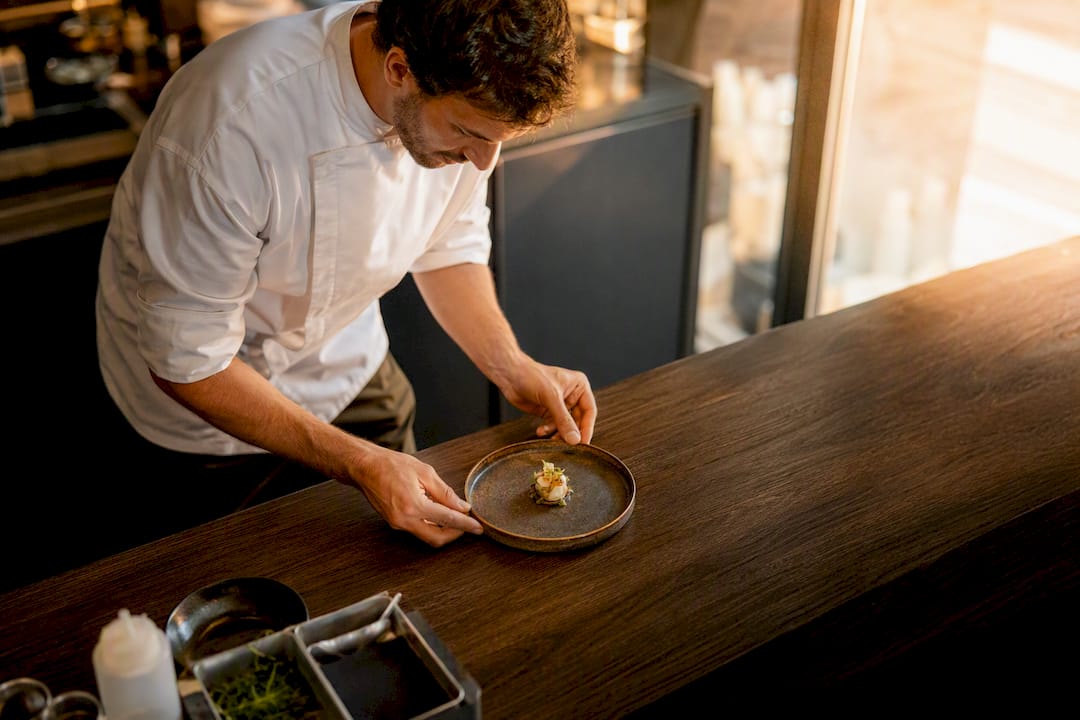 Un chef emplata un aperitivo gourmet en la cocina de un restaurante de alta cocina.