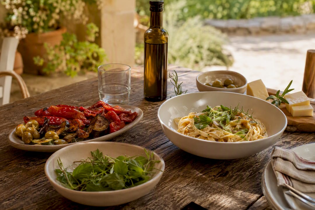 Mesa repleta de pasta fresca al estilo mediterráneo y una variedad de entrantes típicos.