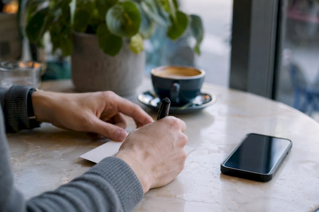 Mains modifiant une note d'adresse près d'un smartphone