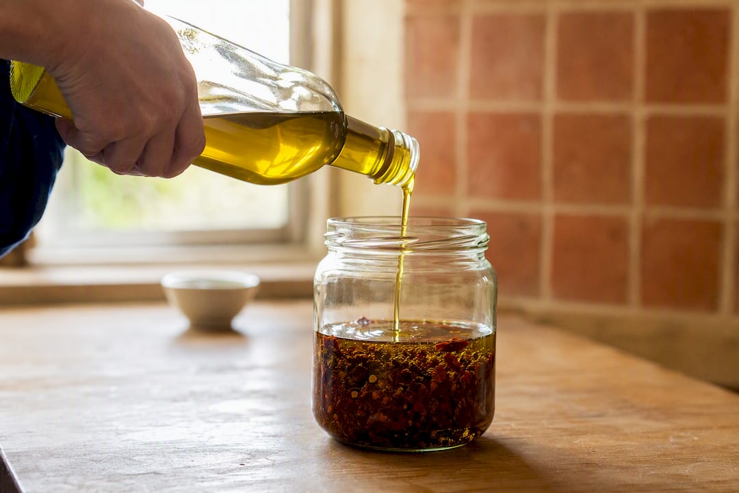 Vertiendo aceite de oliva con hojuelas de chile en frasco