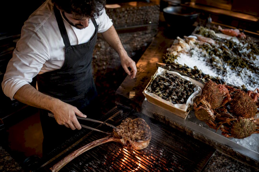 Chef pincelando chuleta tomahawk en la parrilla