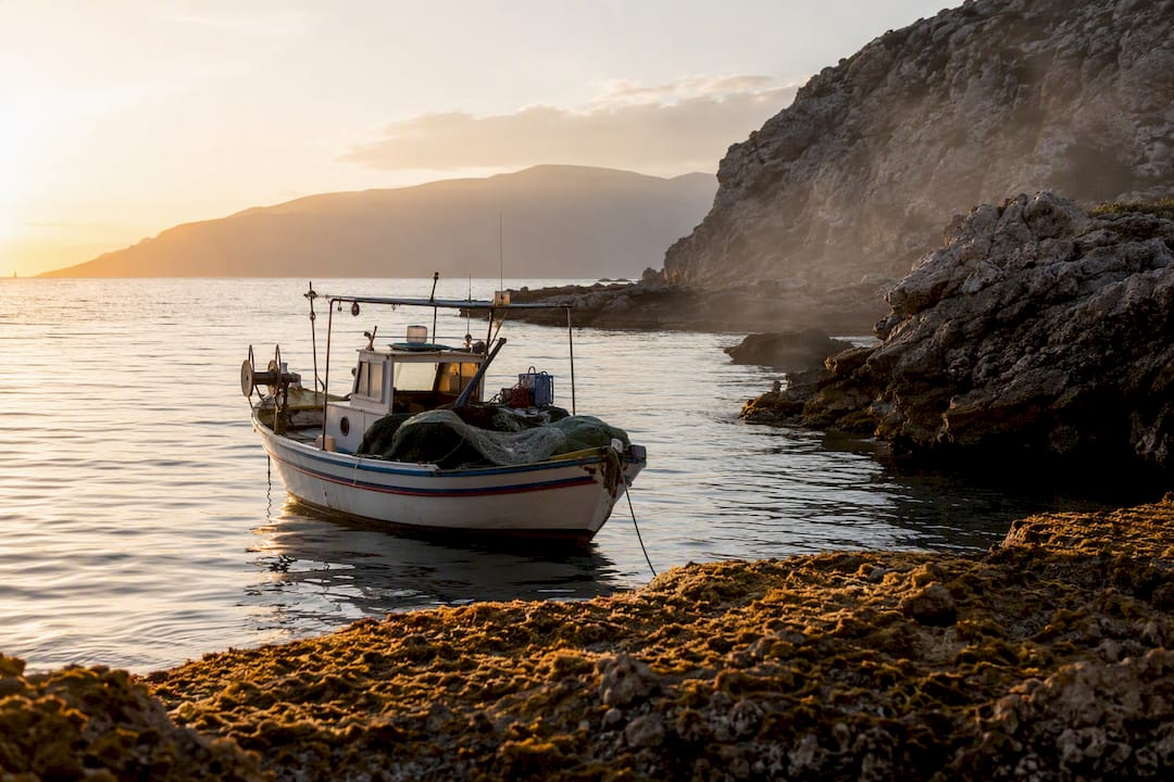 Mediterranean rocky coast with fishing boat at sunrise