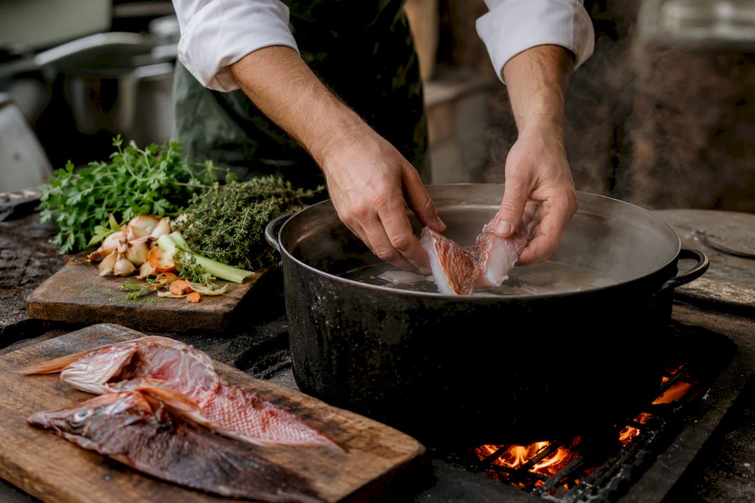 Chef adding fresh rockfish to simmering fumet pot