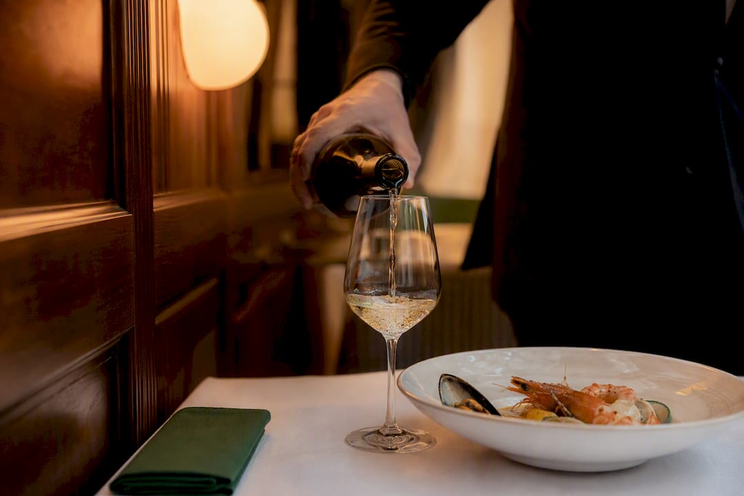 Sommelier pouring wine beside seafood course