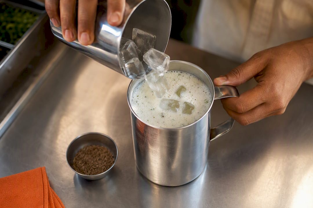 Manos agregando hielo al lassi batido