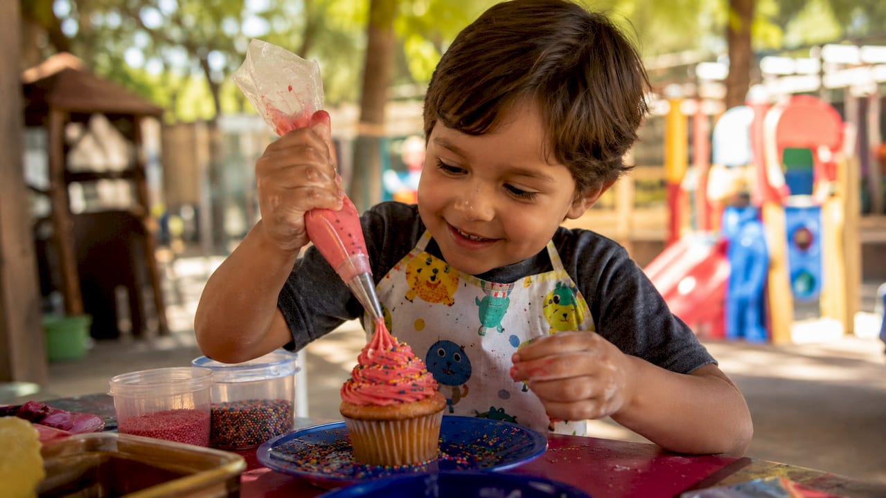 Menino a enfeitar um queque com toppings coloridos