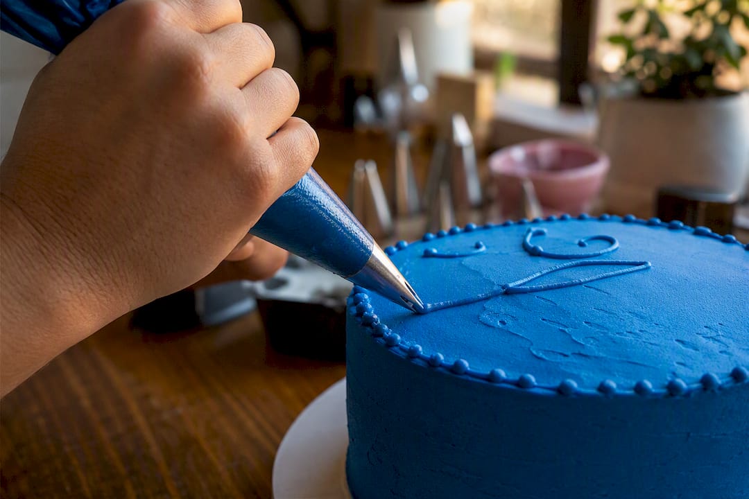 Uma mão a decorar um bolo com uma manga de pasteleiro