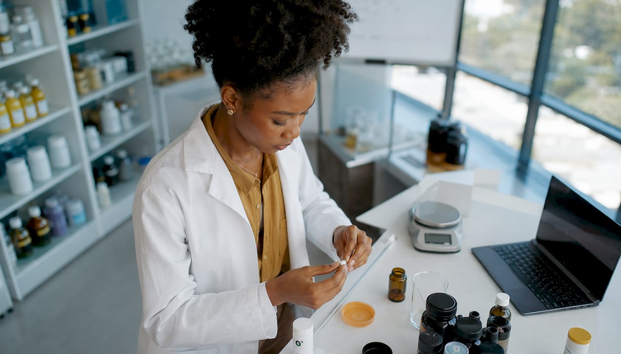 Une chercheuse examine avec précision une capsule de biotine entre ses doigts.