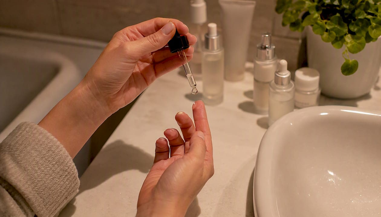 Une main dépose une goutte de sérum sur le bout du doigt avant de l’appliquer sur la peau.